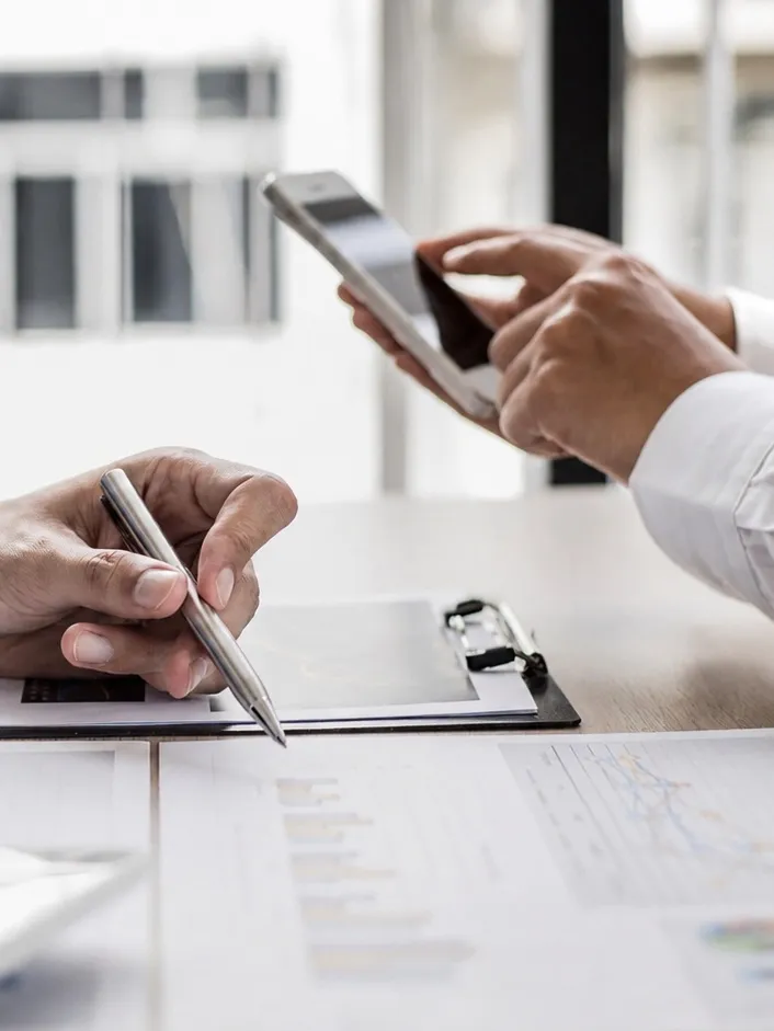 Relevés et pièces d'un dossier repris un à un, stylo en main, un téléphone consulté à côté